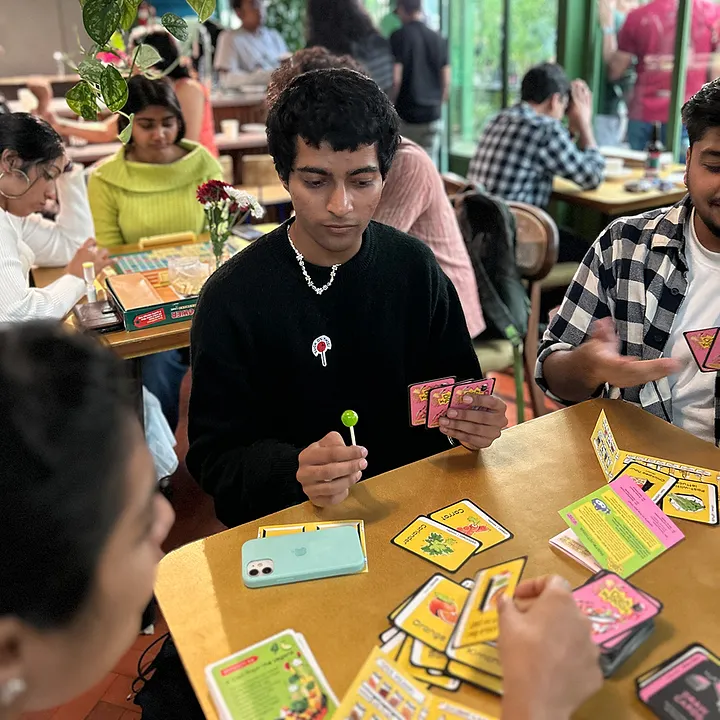 People playing the released Dish Kyaoon game around a table, holding cards and discussing their dishes.