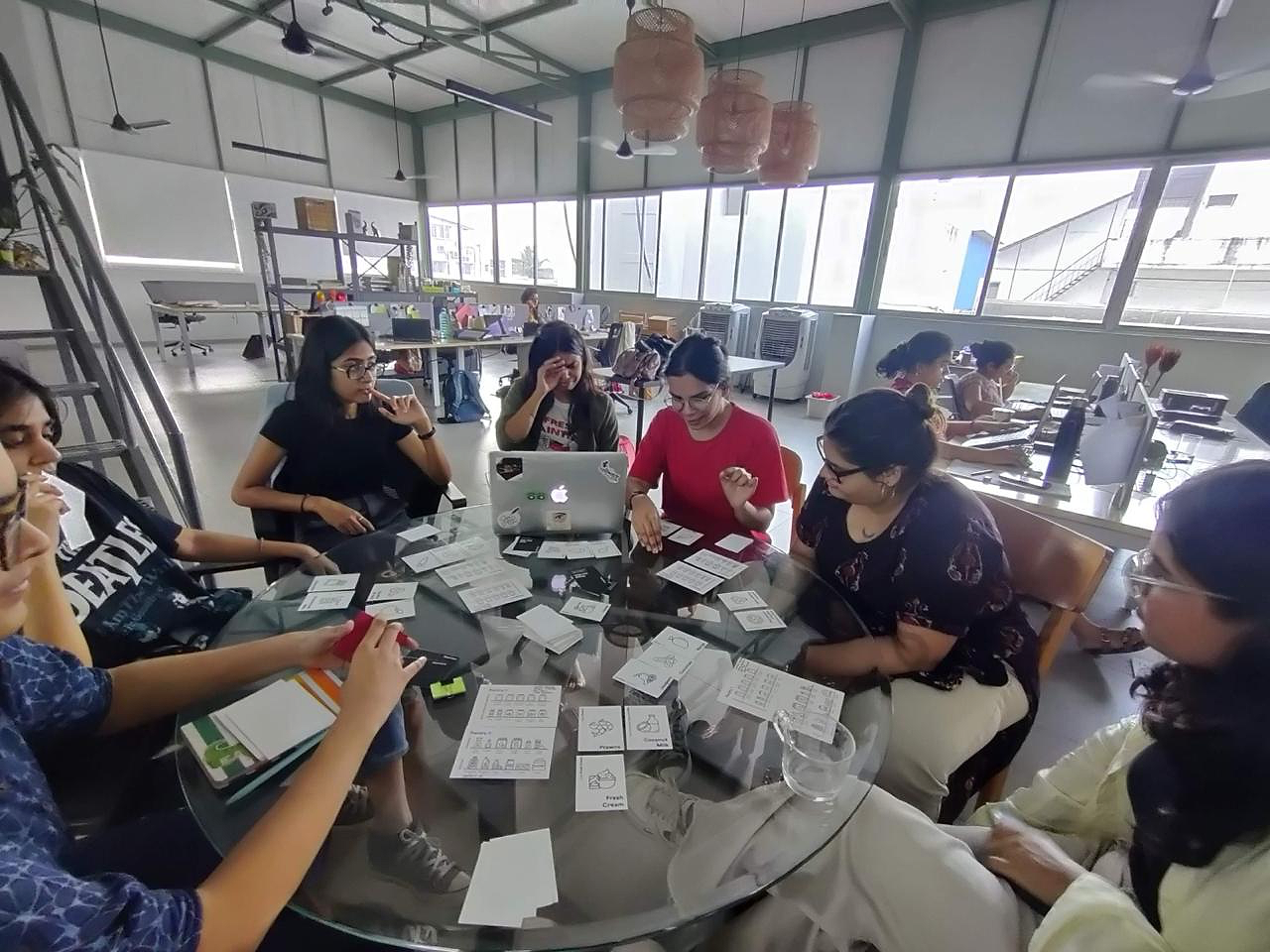 A group gathered around a table testing black-and-white printed game cards, with reference sheets, notes and a laptop.