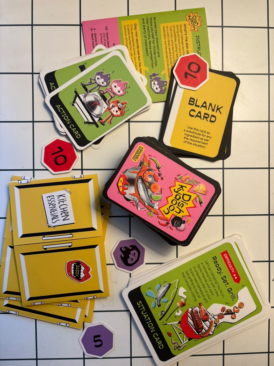 The ingredient and power deck, Dish Don cards, kitchen essentials pantry, tokens and instruction leaflet laid out together.