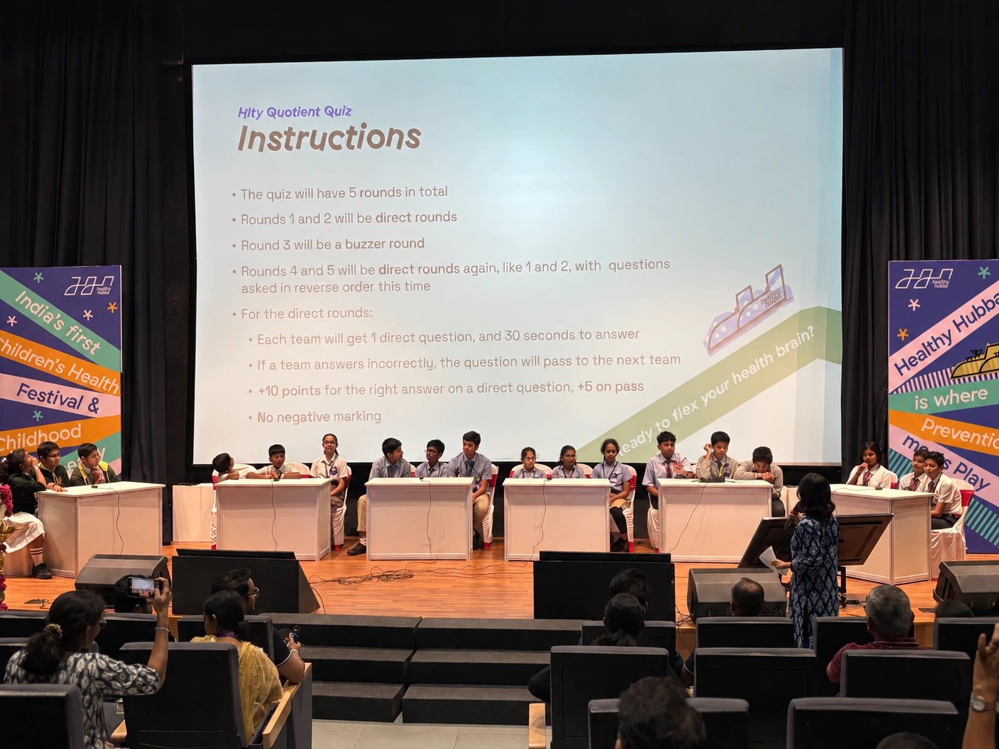 Quiz teams on stage, with the festival announcement and prevention meets play standees installed at either side